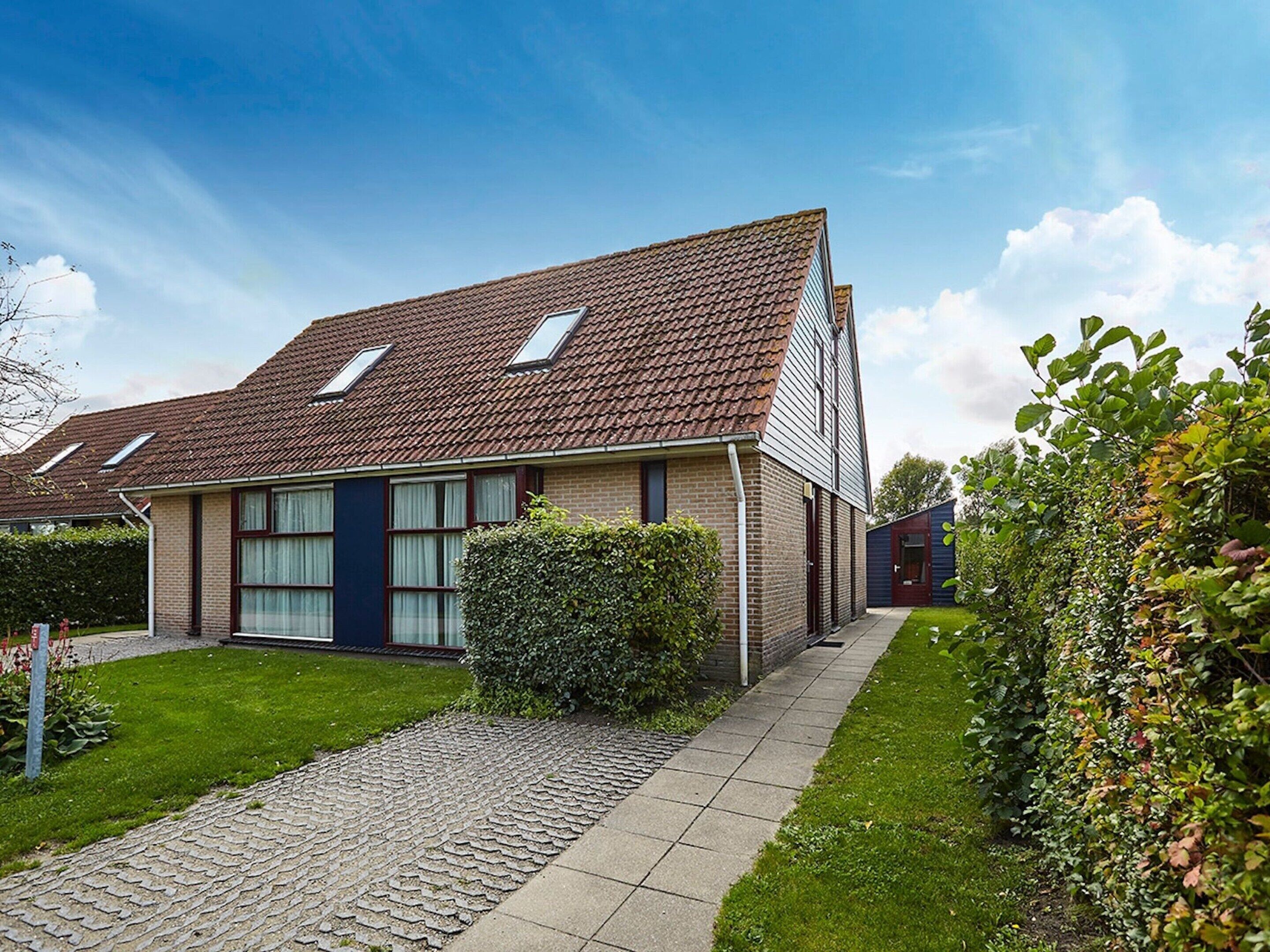 A two-story residential building with a tiled roof, a paved driveway, and a well-maintained lawn.