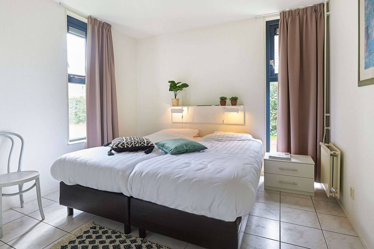 Une chambre à coucher avec un lit, une table de chevet, une chaise et une fenêtre avec des rideaux.
