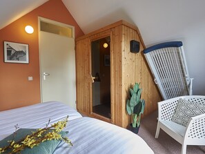 A bedroom with a bed, a wooden door, a white chair, and a potted plant.