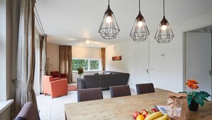 Uma área de jantar moderna com mesa de madeira, cadeiras e luminárias pendentes.