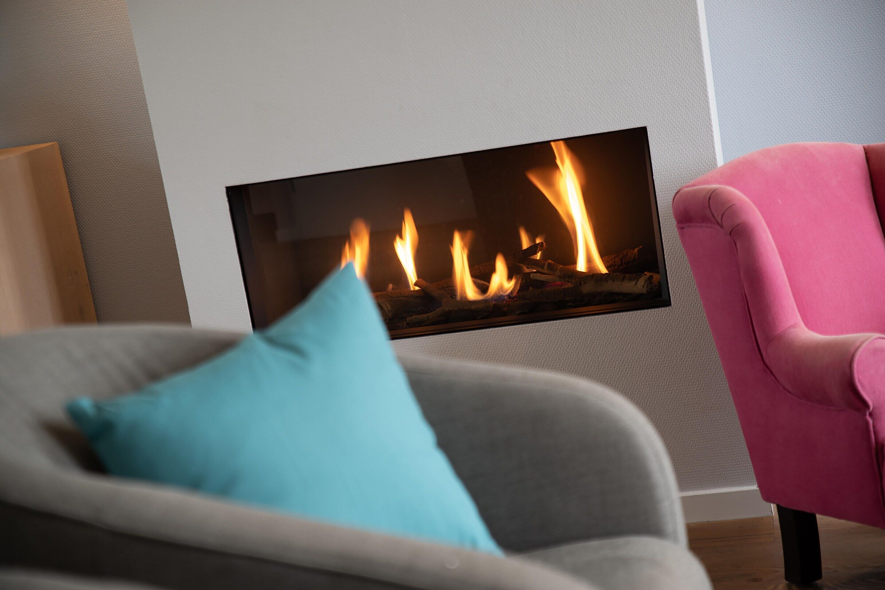 A modern living room with a fireplace, a grey sofa, a blue pillow, and a pink armchair.