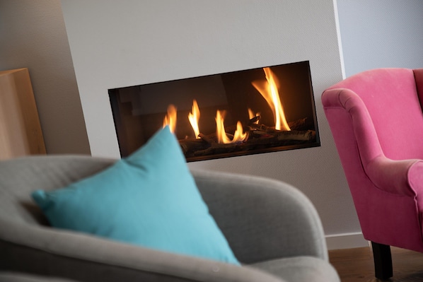 A modern living room with a fireplace, a grey sofa, a blue pillow, and a pink armchair.