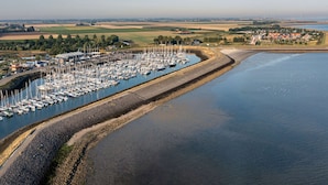 An aerial view of a marina with numerous boats docked, surrounded by a coastal landscape with fields and a small village. - Holiday Home With Whirlpool and Sauna in a Quiet Area in Zeeland (Colijnsplaat)