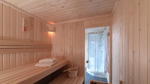 A sauna room with wooden benches, a wooden bucket, and a shower area. - Holiday Home With Whirlpool and Sauna in a Quiet Area in Zeeland (Colijnsplaat)