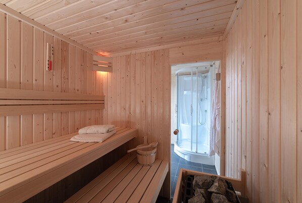 Sala de sauna con bancos de madera, un balde de madera y zona de ducha.