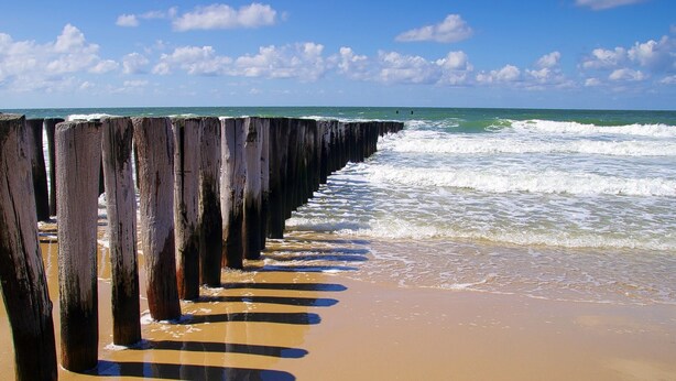A wooden pier extending into the ocean with waves crashing against it. - Holiday Home With Whirlpool and Sauna in a Quiet Area in Zeeland (Colijnsplaat)
