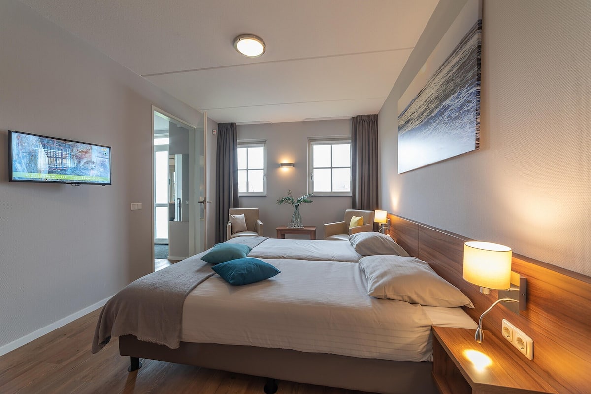 Une chambre d’hôtel avec un lit, des tables de chevet, une télévision et un tableau au mur.