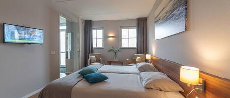 A hotel room with a bed, bedside tables, a TV, and a painting on the wall.