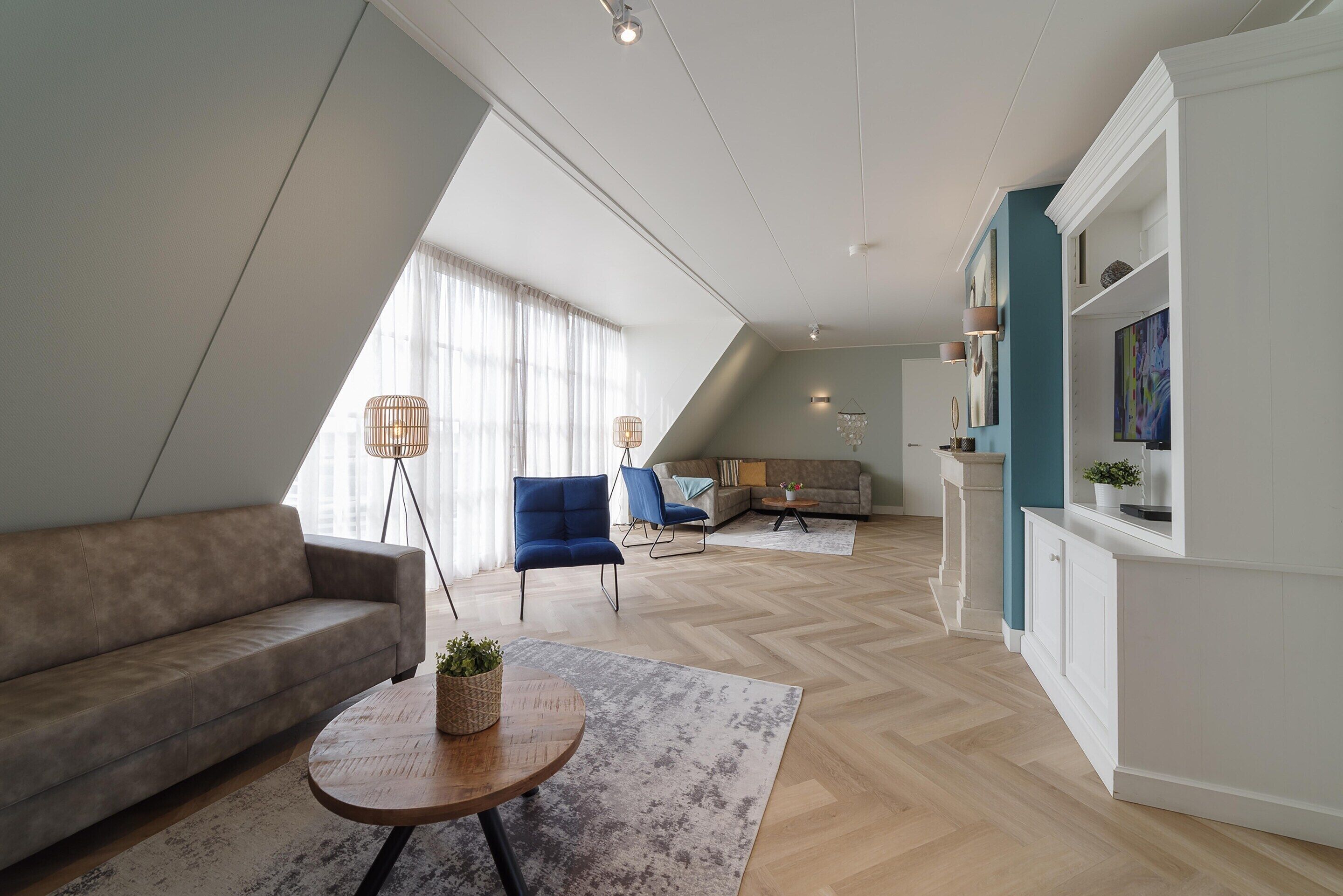 Uma sala de estar moderna com um sofá, uma mesa de centro e uma poltrona azul. Um tapete com padrão herringbone cobre o chão.