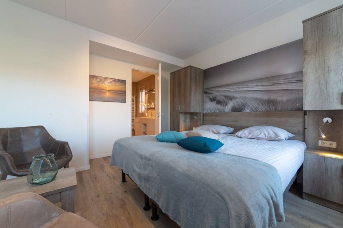 Une chambre moderne avec un grand lit, une tête de lit en bois et une armoire en verre.