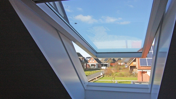 Une fenêtre de toit donnant sur des maisons d’habitation et des panneaux solaires.