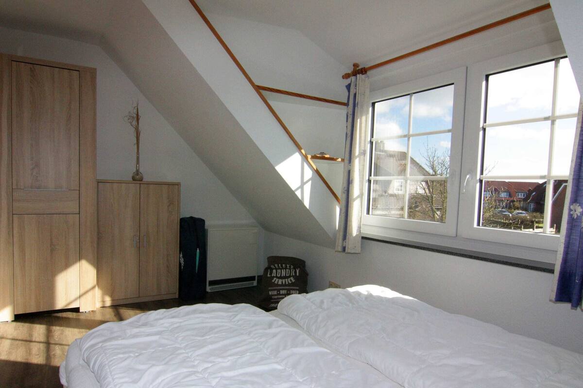 A bedroom with a sloped ceiling, a bed, a wardrobe, and a window with a view of houses outside.