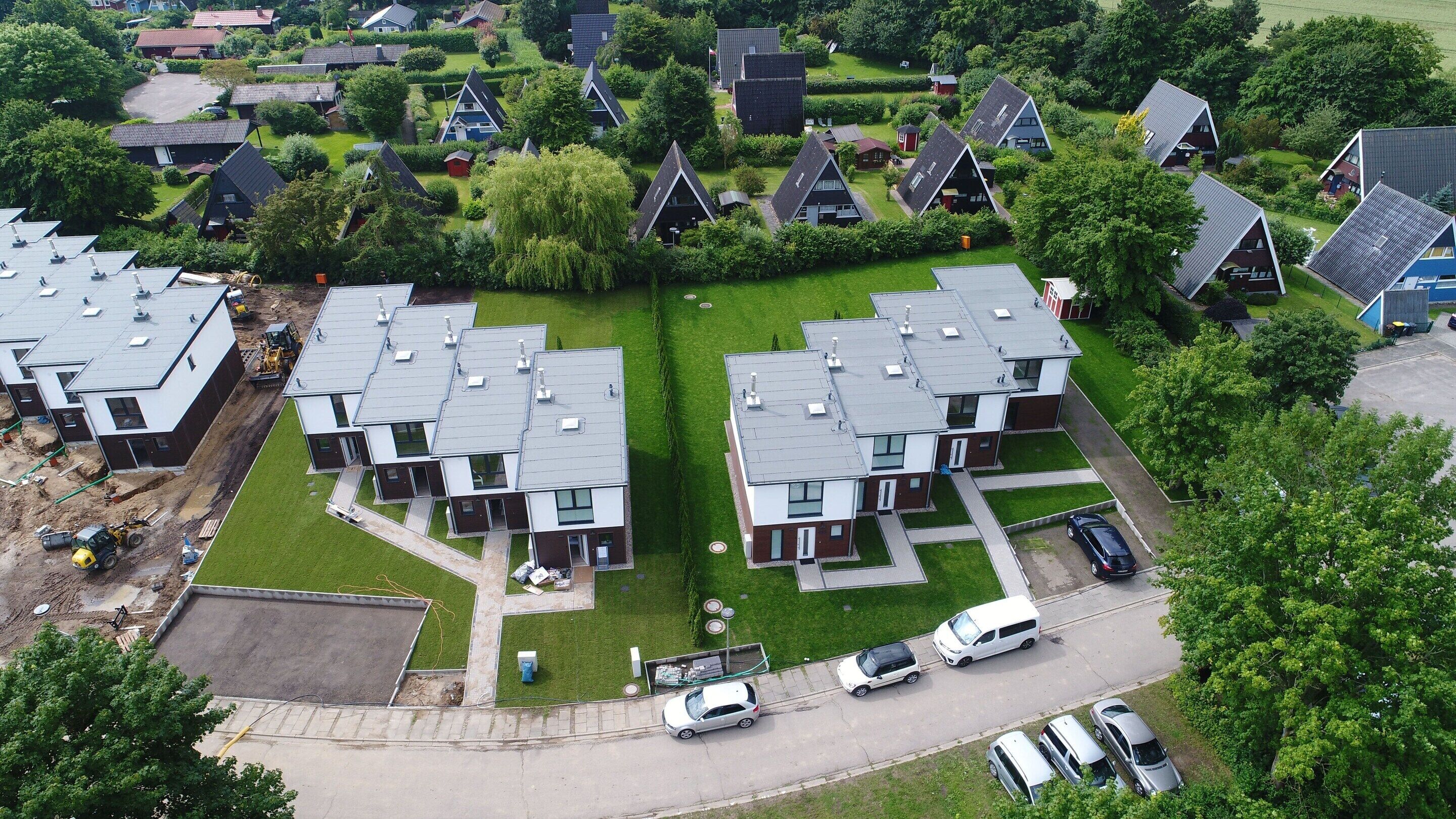 Ein Wohngebiet mit modernen Häusern, einer zentralen Grünfläche und einem Parkplatz mit Autos.