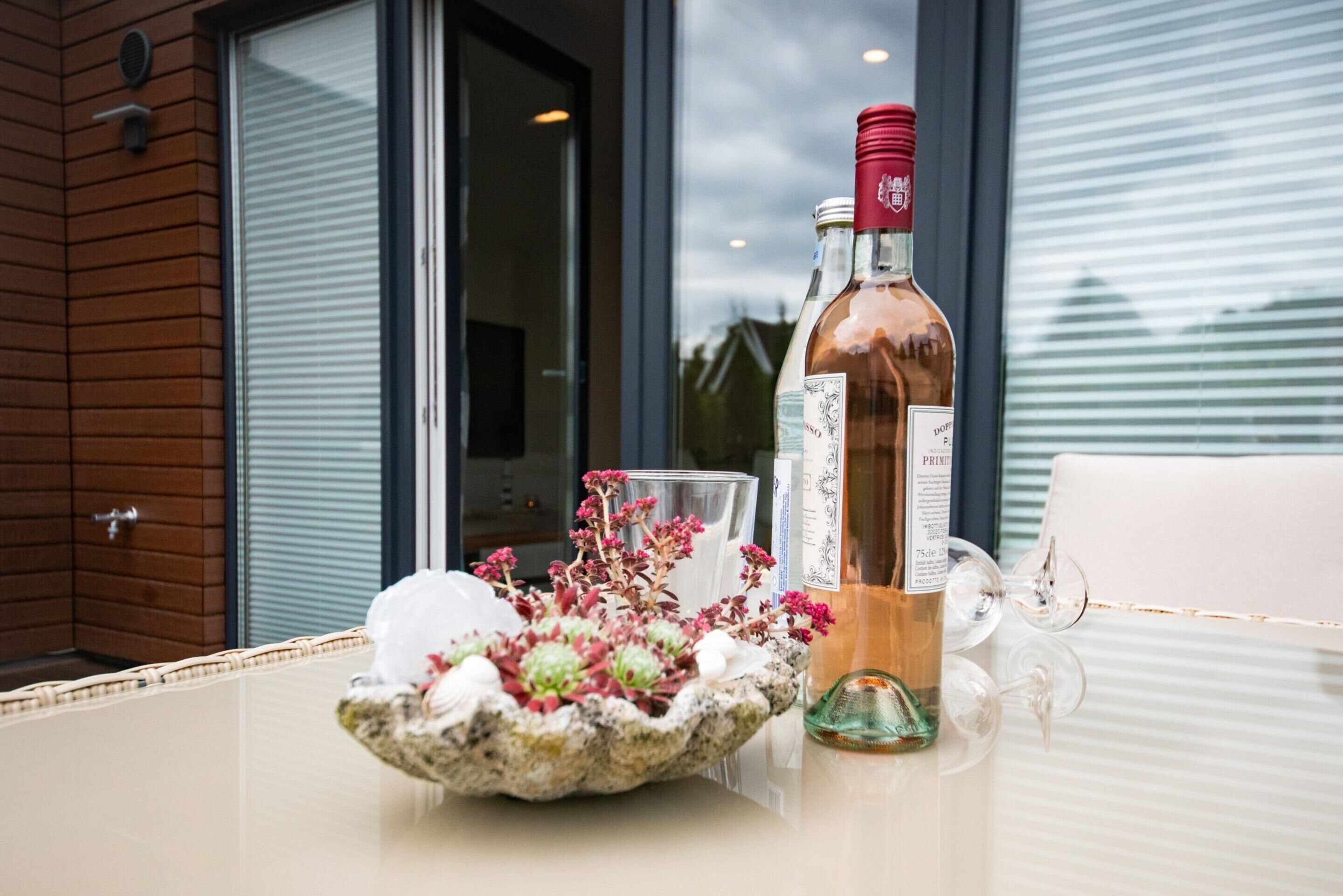 Una mesa con una botella de vino, una copa y un cuenco decorativo con flores.