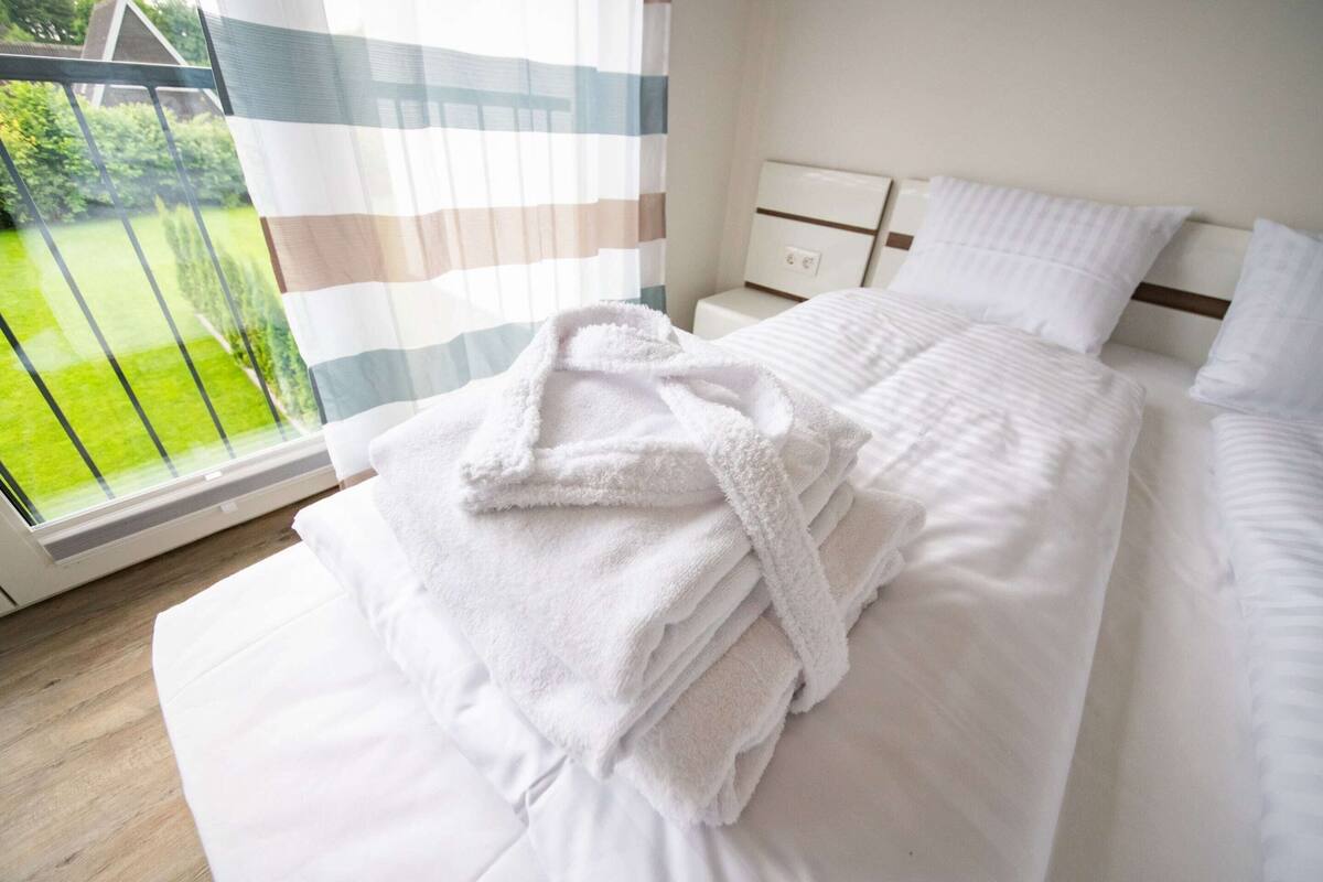 Habitación de hotel con cama, mesita de noche y ventana que da a un jardín verde.