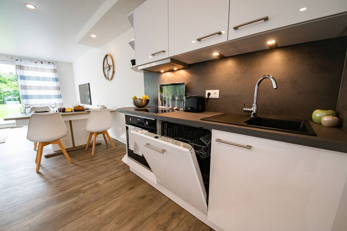Cocina moderna con armarios blancos, lavavajillas integrado, pileta y un comedor con dos sillas.