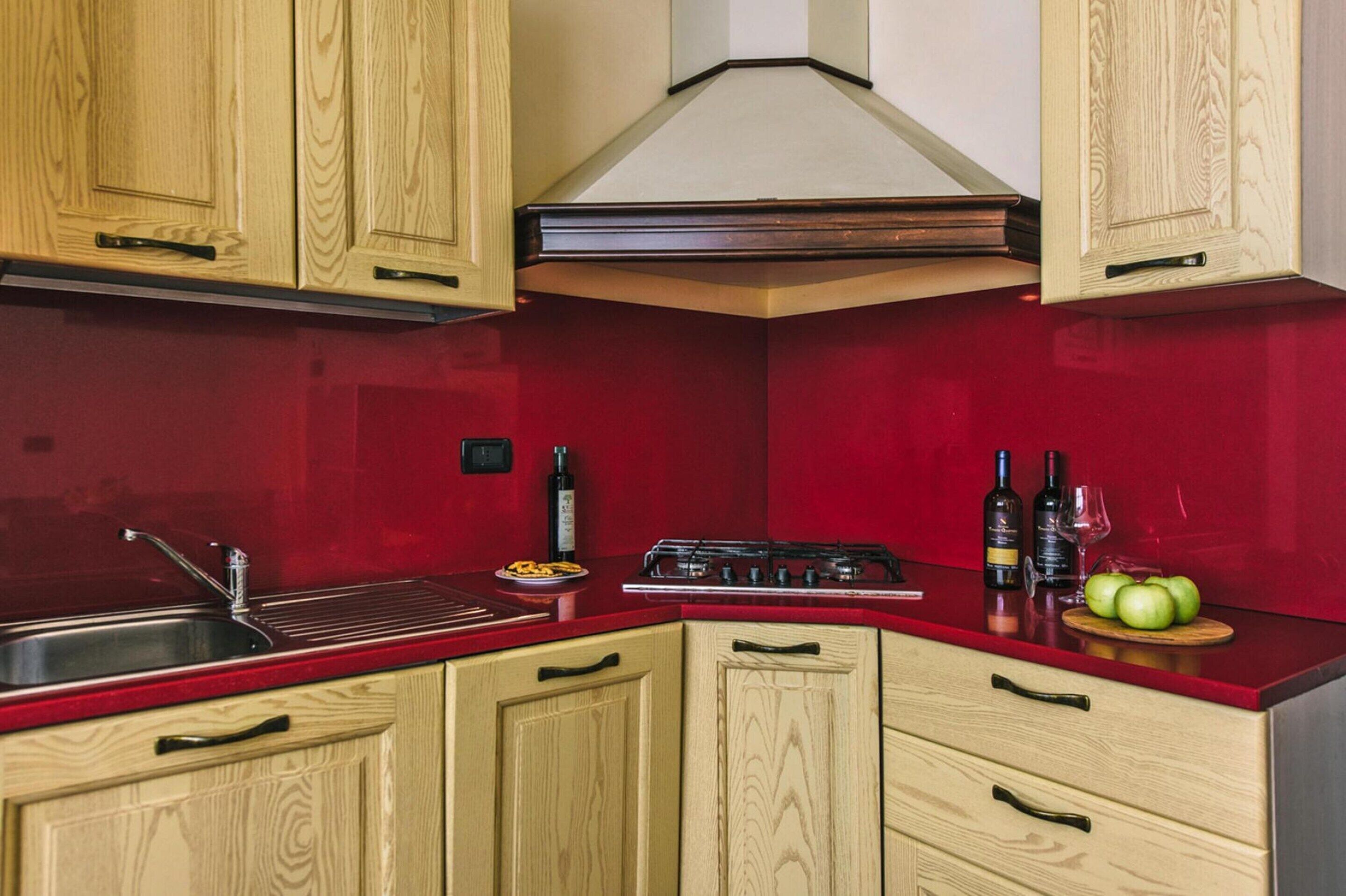 A kitchen with wooden cabinets, a red backsplash, a gas stove, and a sink.