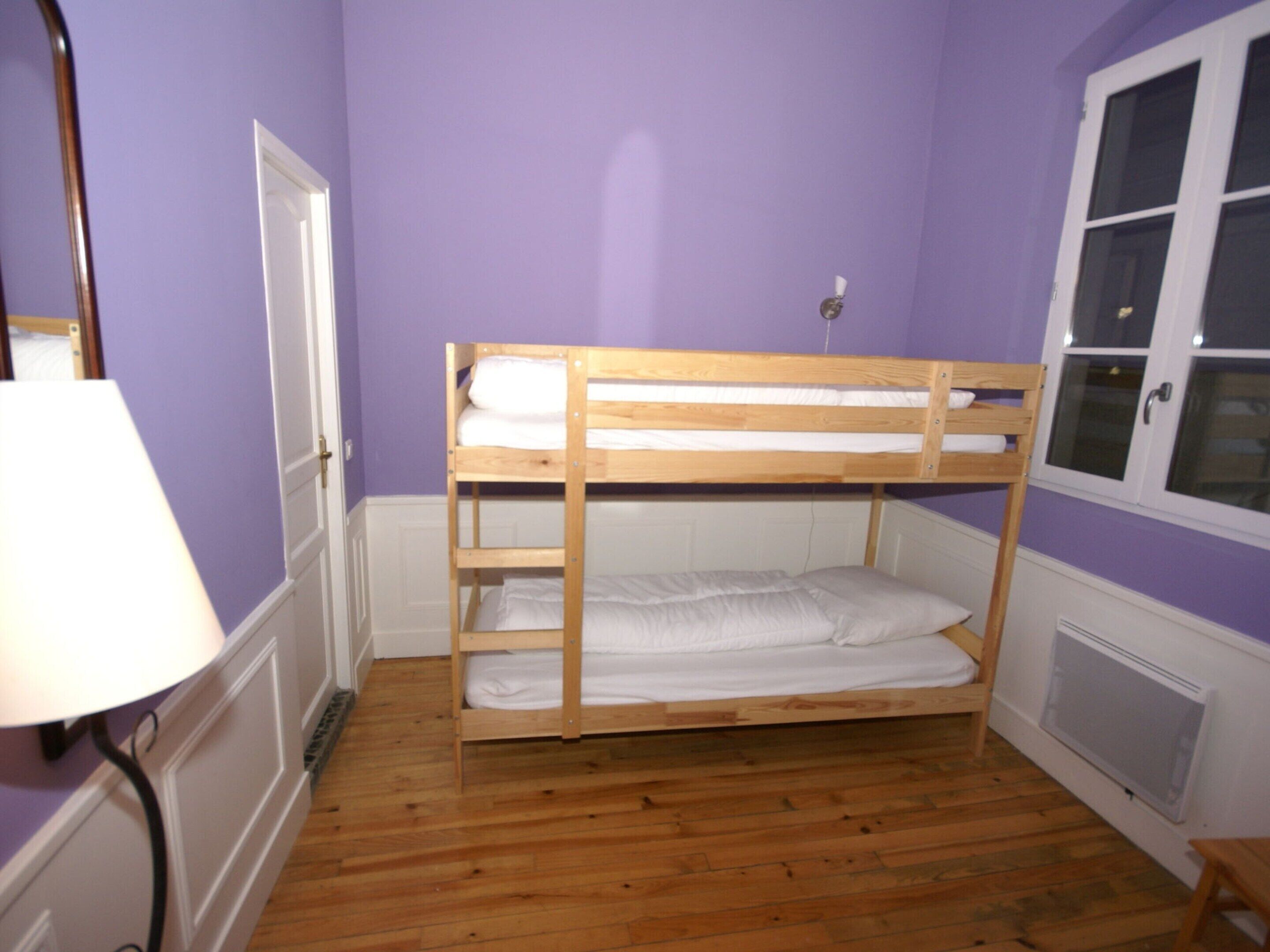 A bunk bed in a room with purple walls and wooden flooring.