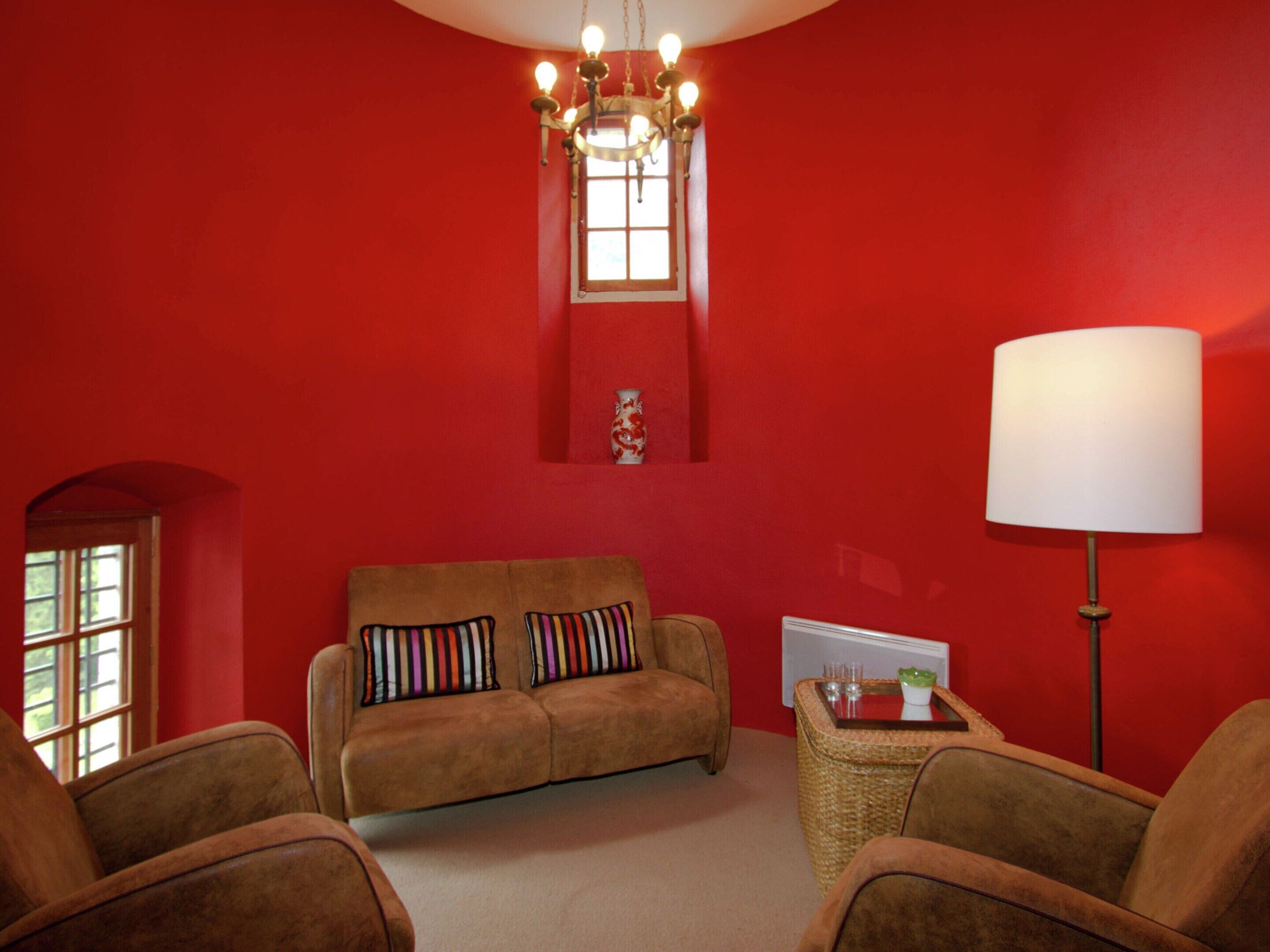 Una habitación con una pared roja, un sofá marrón con almohadones a rayas, una lámpara y una mesita con vasos.