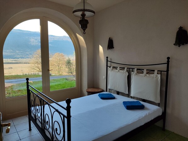 A bedroom with a bed, a window with a view of the countryside, a lamp, and a wall-mounted light fixture. - Charming Castle in Serrieres-en-chautagn With Pool (Serrieres-en-Chautagne)