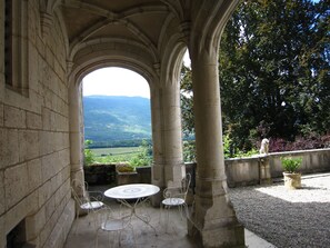 A stone archway leading to a patio with a table and chairs, overlooking a scenic valley.