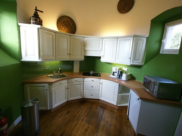 A kitchen with white cabinets, a wooden countertop, a sink, a kettle, a coffee maker, a toaster, and a microwave.