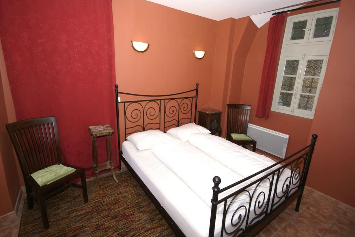 Een slaapkamer met een bed, een stoel, een nachtkastje en een raam.