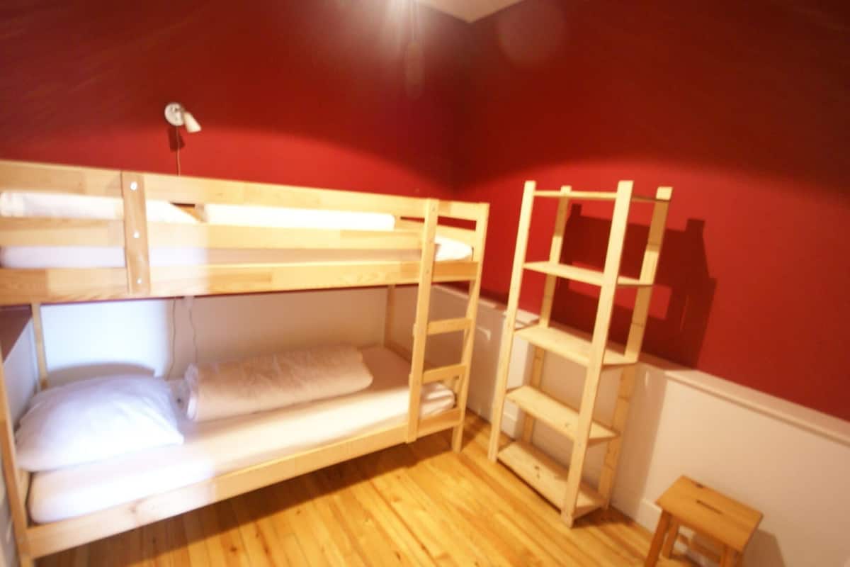 Een slaapkamer met een stapelbed, een rode muur, houten vloer en een klein houten krukje.