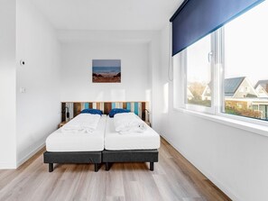 A modern bedroom with two beds, a large window with a view of houses, and a beach painting on the wall. - Serene Holiday Home in De Koog Texel With Sauna (De Koog)