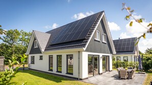 Une maison moderne dotée de panneaux solaires, d’un patio avec mobilier d’extérieur et d’une pelouse bien entretenue.