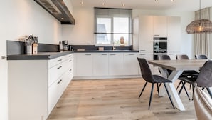 Une cuisine moderne avec des meubles blancs, un plan de travail en bois et un coin repas comprenant une table et des chaises en bois.