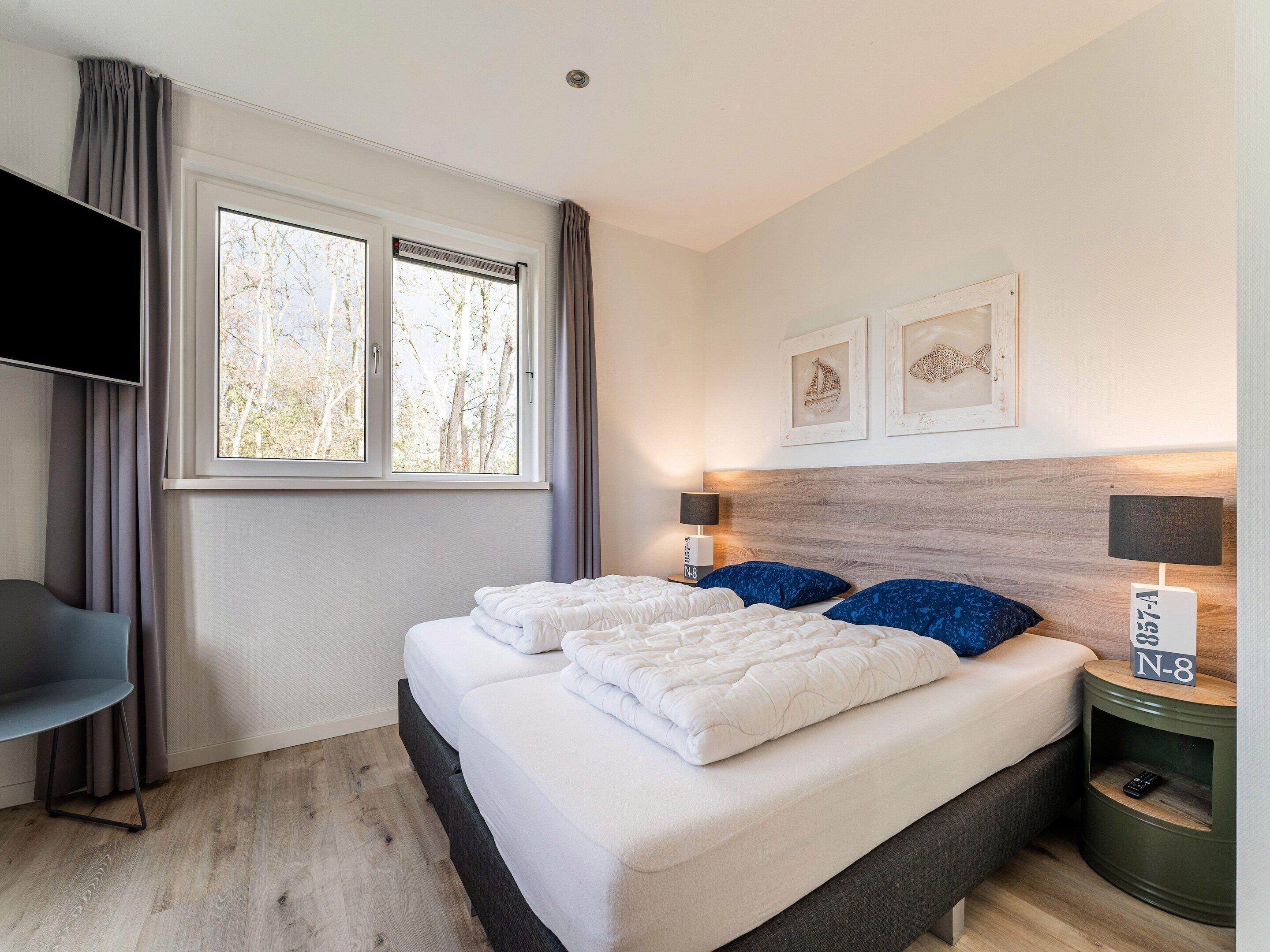 A bedroom with a bed, a TV, a nightstand, and a window with curtains.