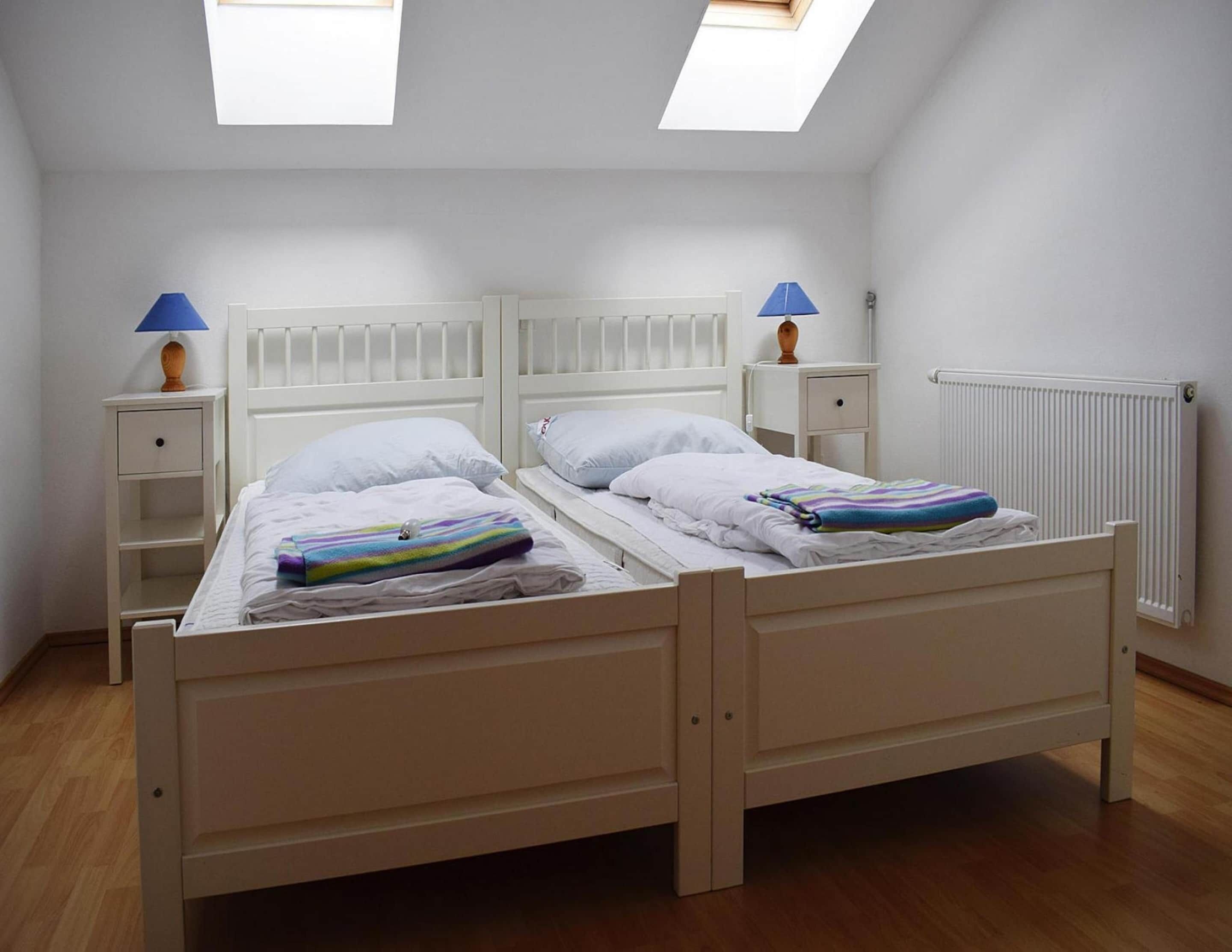 A twin room with two beds, a skylight, a radiator, and a nightstand with a lamp.