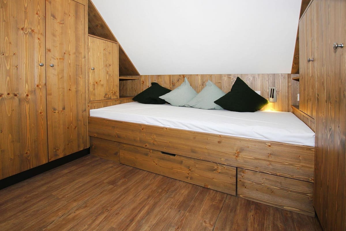 Un dormitorio estilo loft con techo de listones de madera, una cama con almohadas y cajones de madera empotrados.