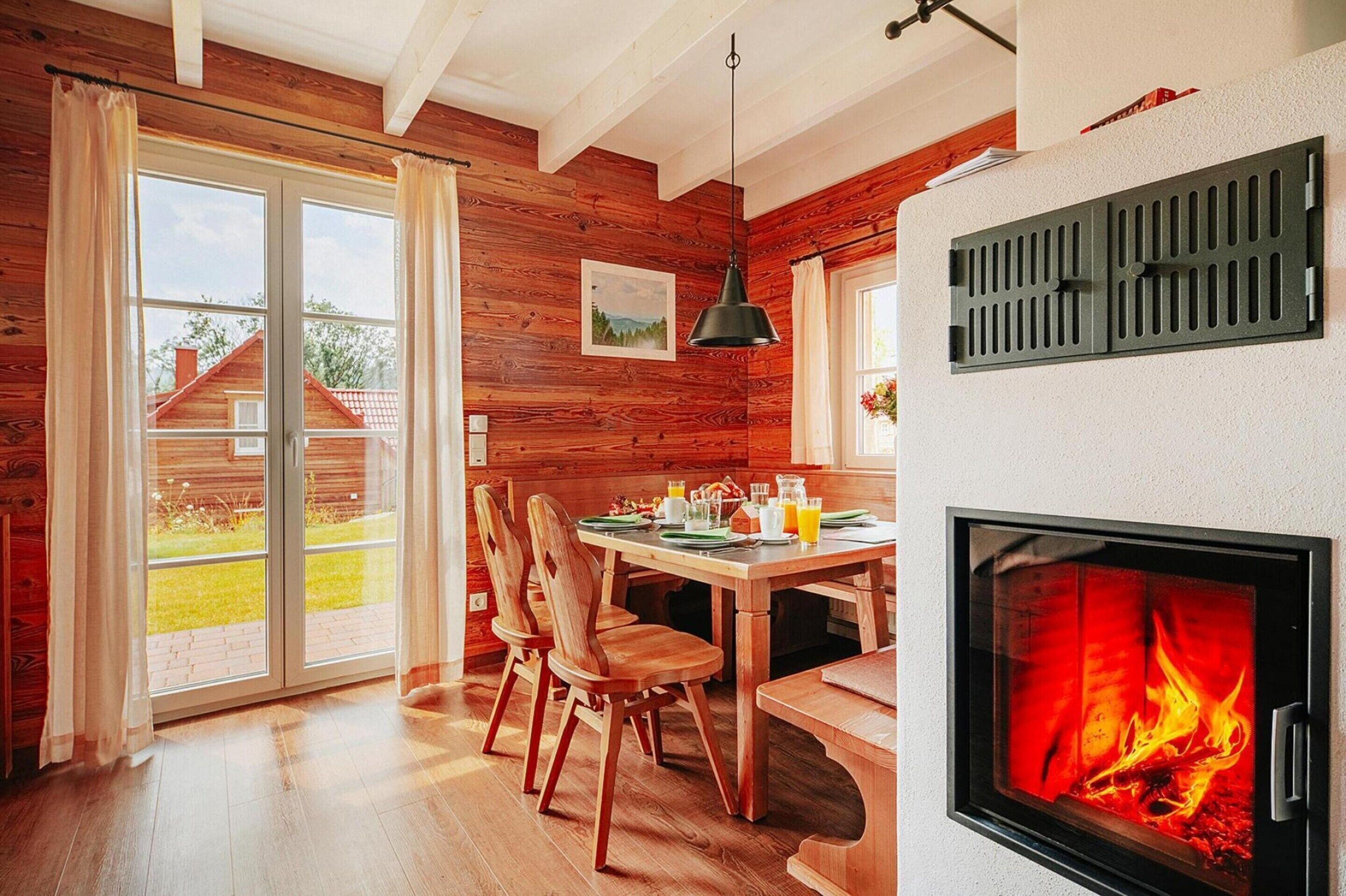 Un interior acogedor de madera con comedor, chimenea y puerta corrediza de vidrio que da a un jardín.