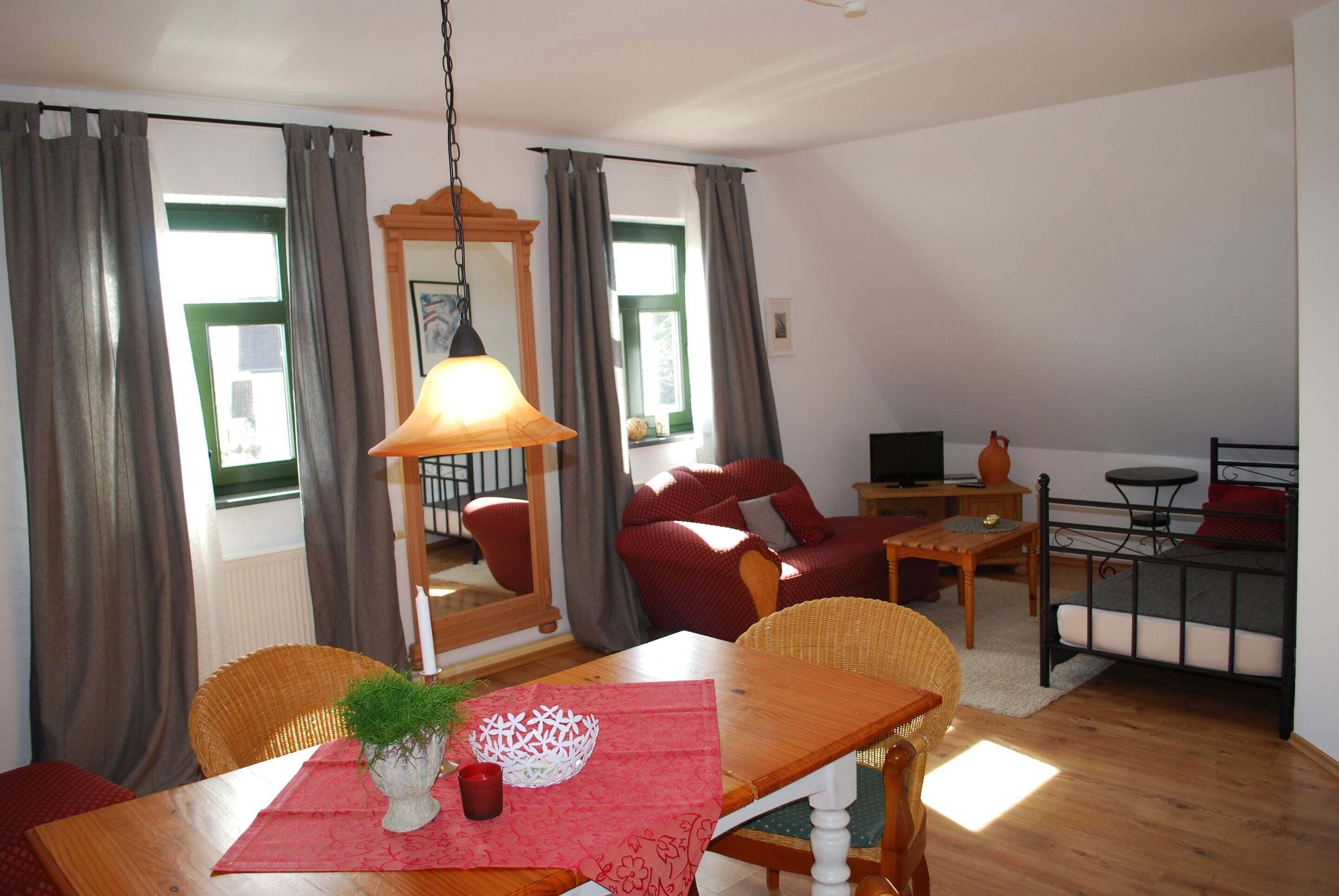 Una sala de estar acogedora con comedor, que incluye una mesa de madera, sillas de mimbre, un sofá rojo y un televisor sobre una mesita.