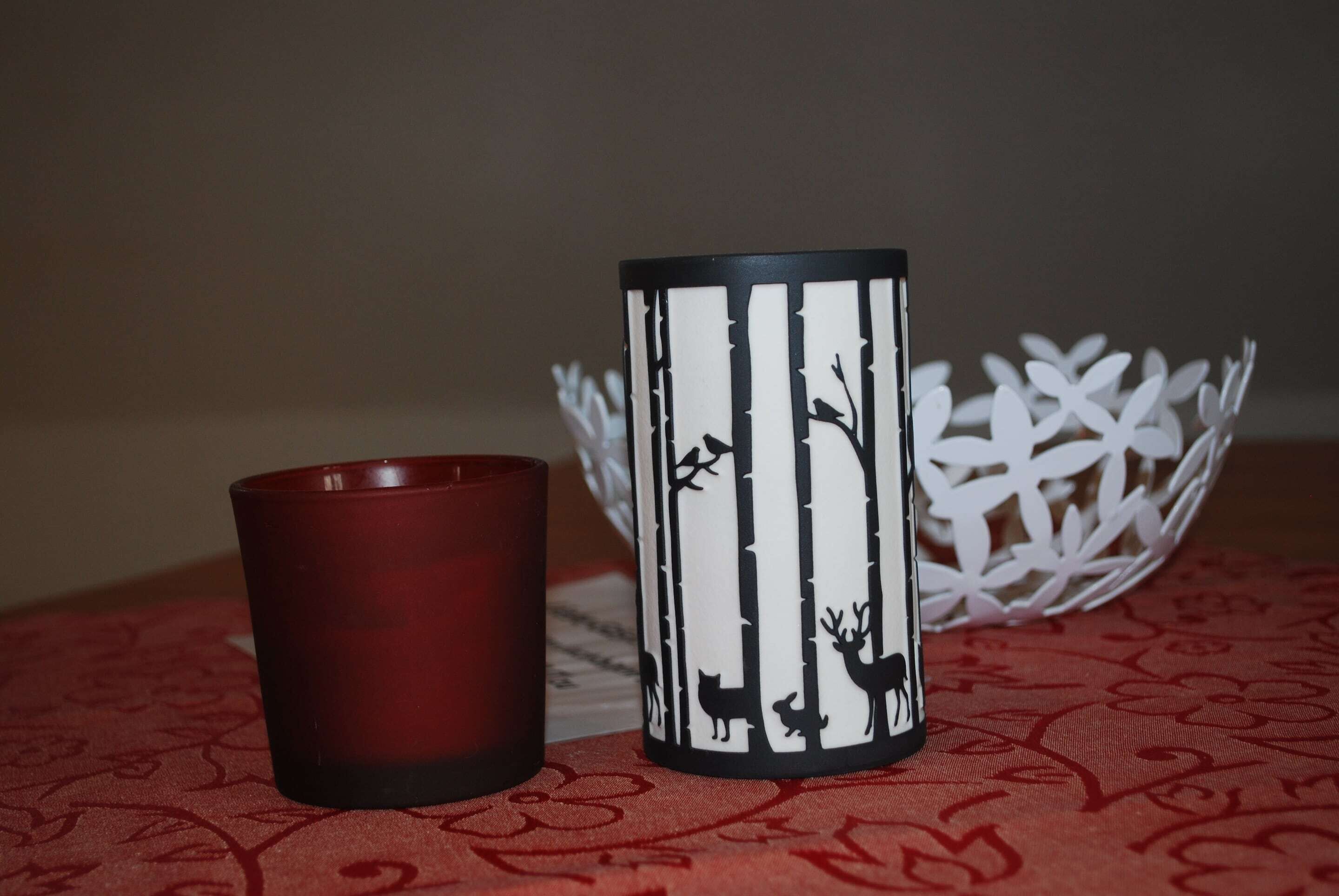 A red candle and a decorative candle holder with a forest and deer design.