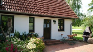 A white house with a brown tiled roof, a front door, and a small outdoor seating area with two wooden tables and four chairs. - Grosses Landhaus mit Swimmingpool in Dargun (Dargun)