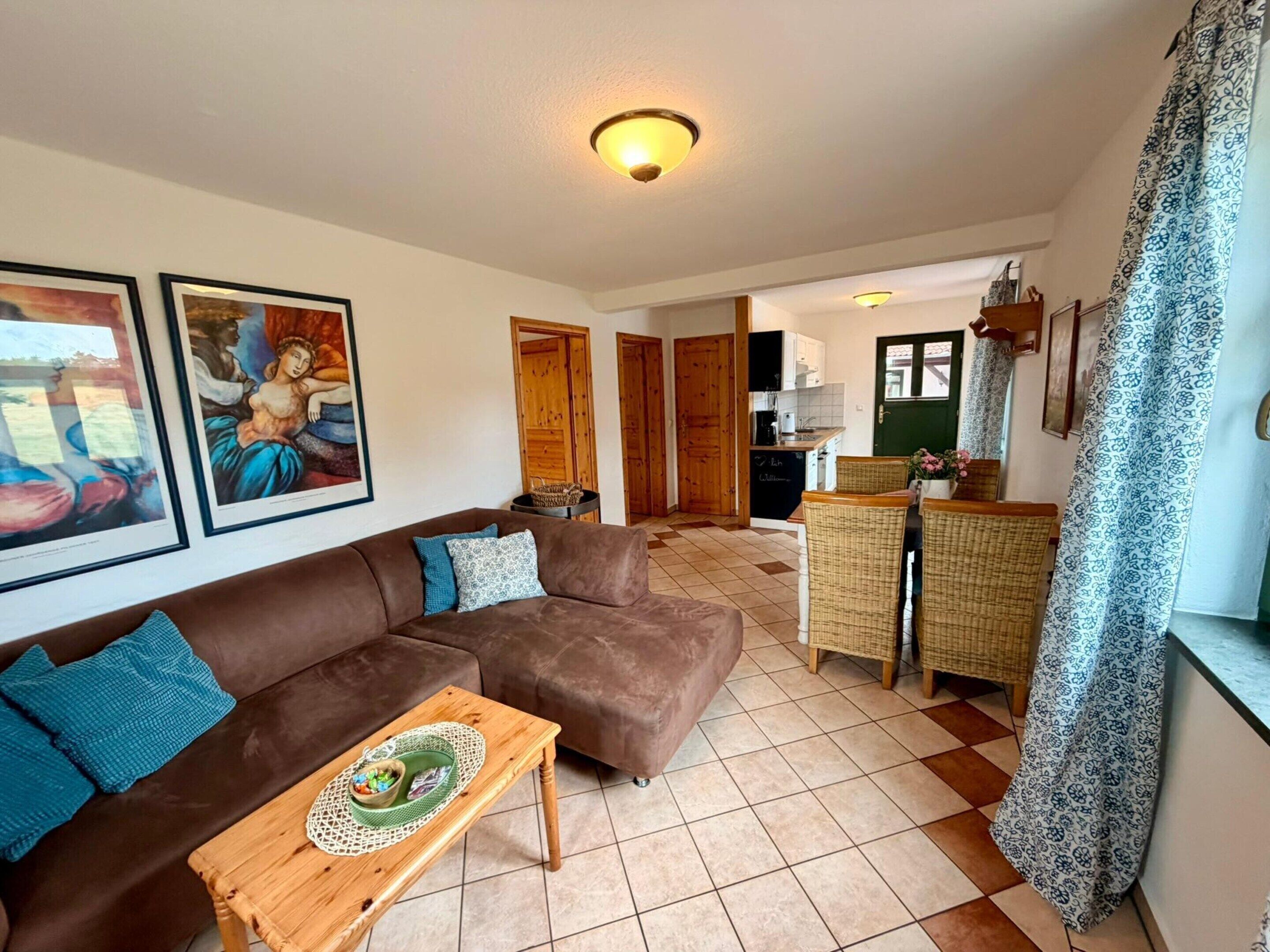 A living room with a brown sofa, a wooden coffee table, and a kitchen in the background.