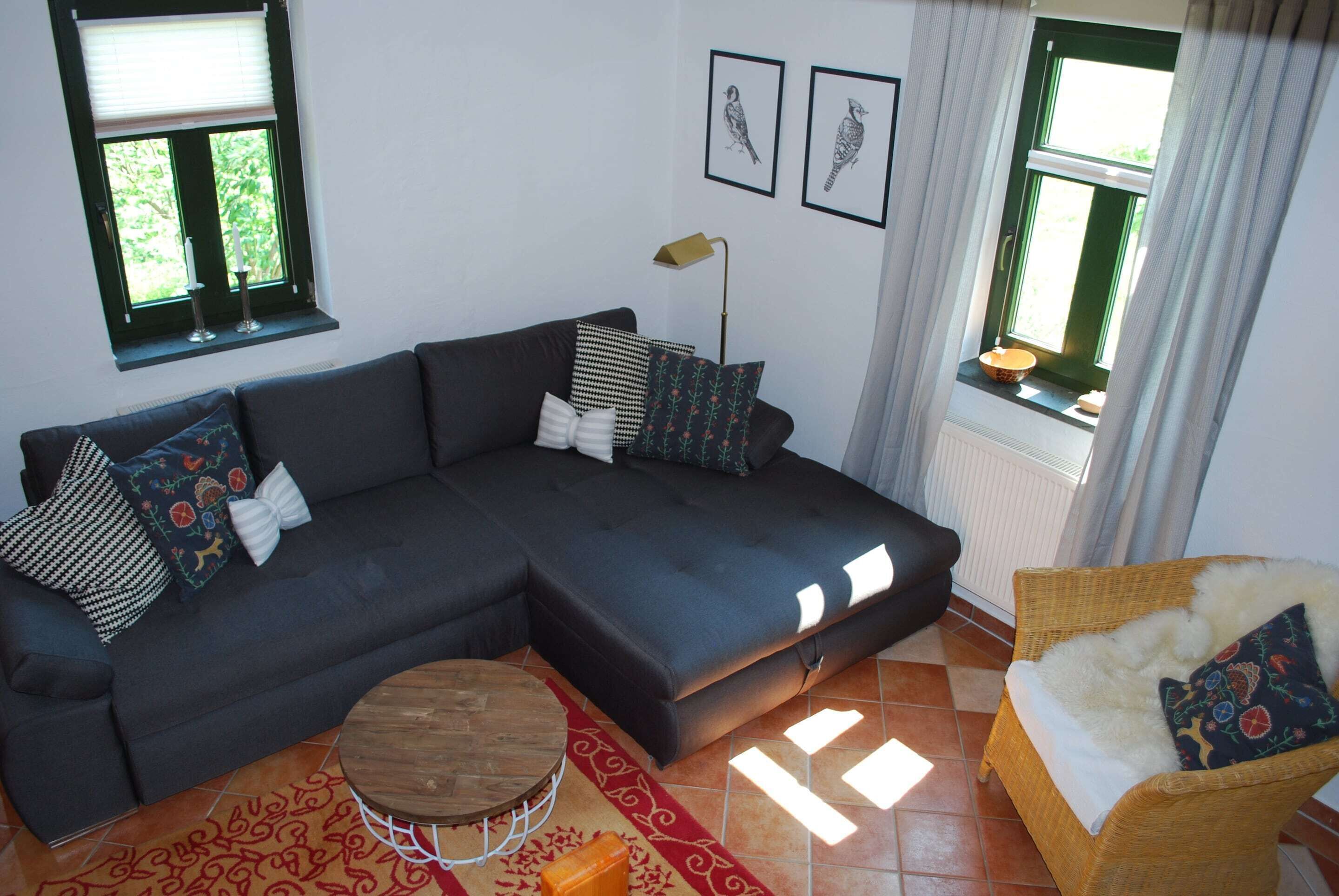 A living room with a dark-colored sectional sofa, a round wooden coffee table, a wicker armchair, and a patterned rug.