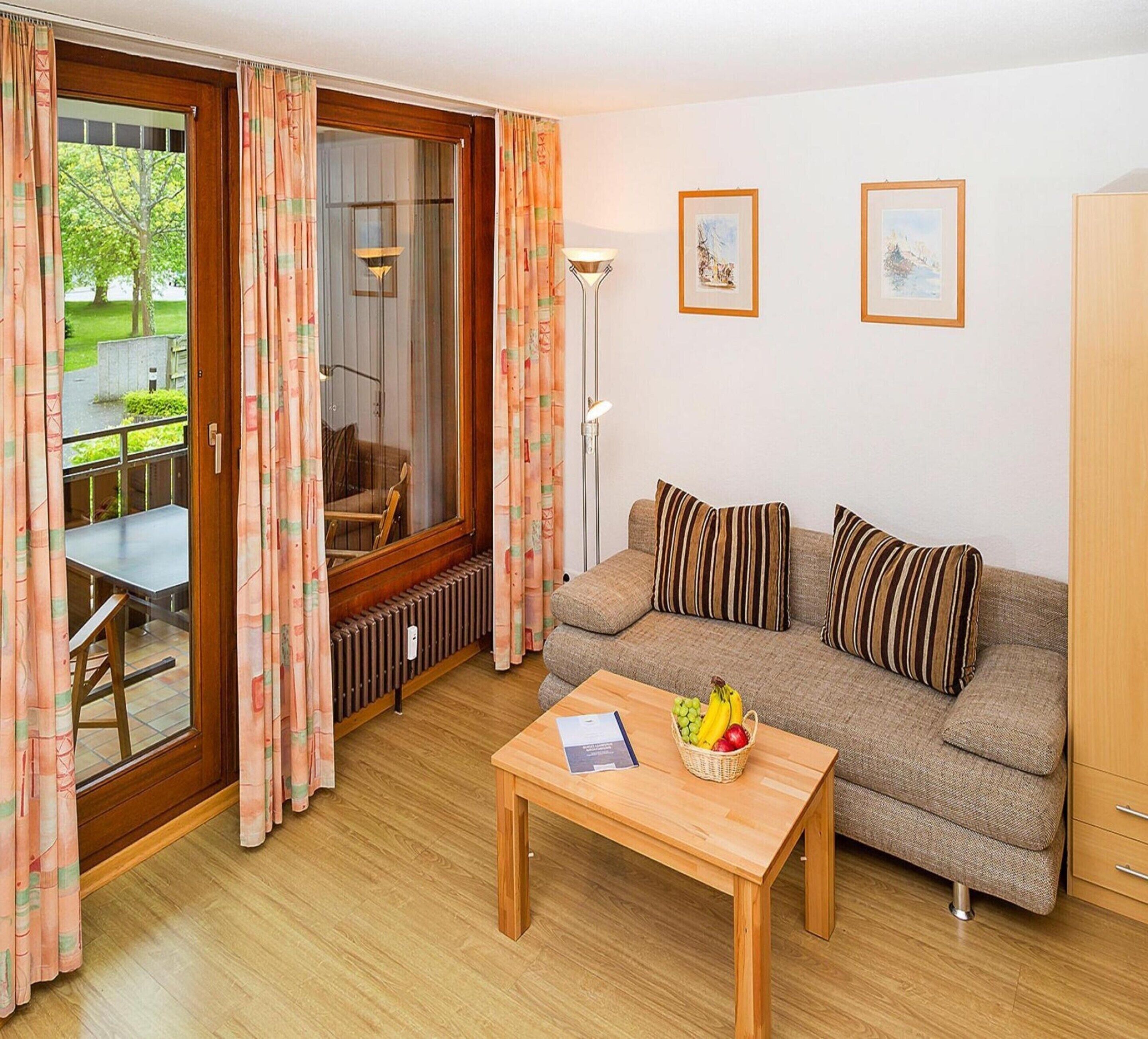 Una sala de estar acogedora con un sofá, una mesa baja con fruta y vistas al exterior a través de un ventanal corredera.
