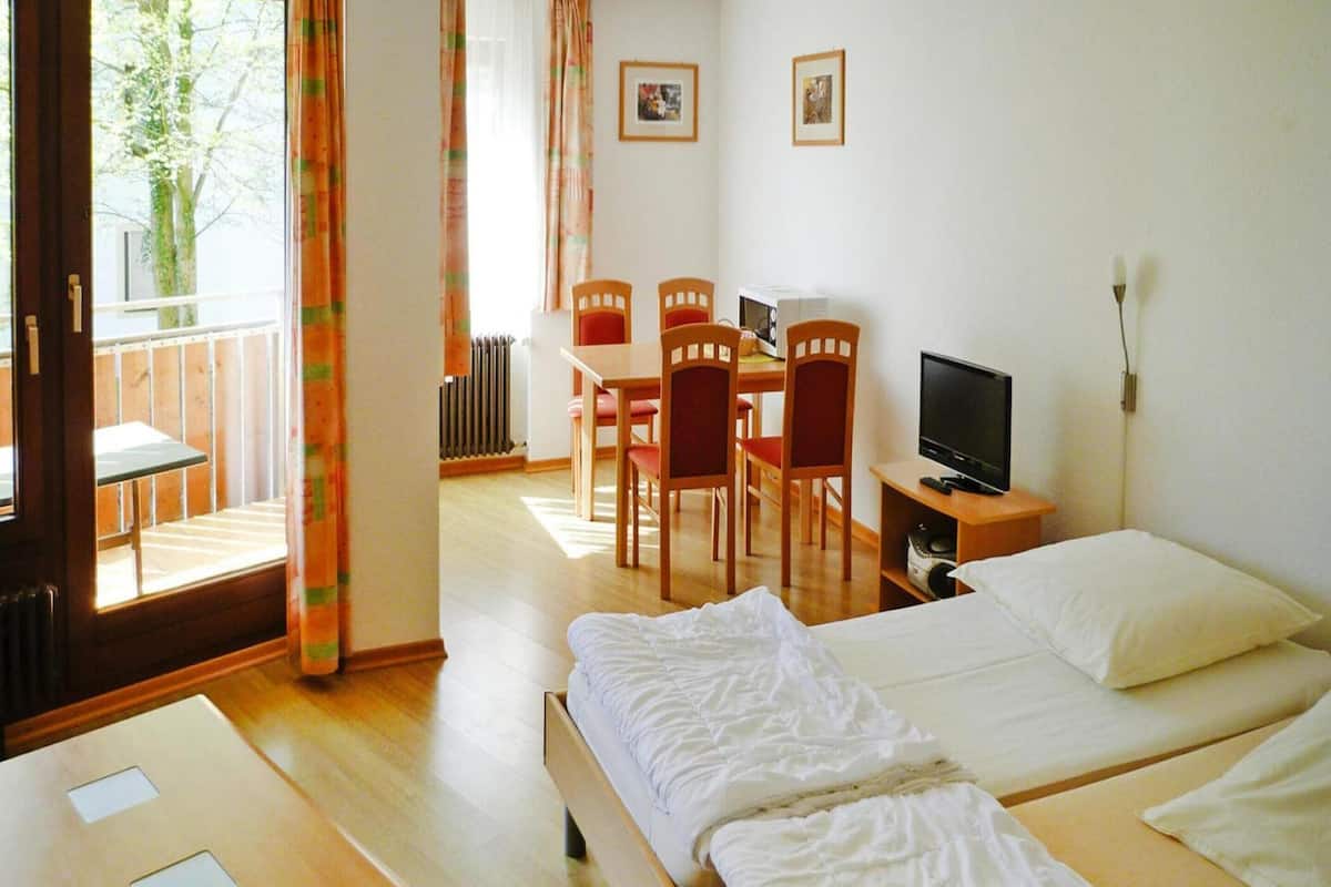 A hotel room with a bed, a desk, a chair, a TV, and a view of the outdoors.