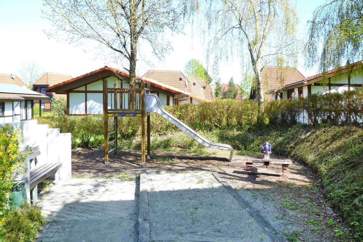 A playground with a slide, surrounded by a landscaped area with trees and bushes.