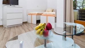 Ett modernt hotellrum med en säng, en TV, ett glasbord med frukt och utsikt över träd.