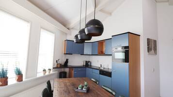 A modern kitchen with blue cabinets, a wooden dining table, and pendant lights.