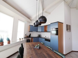 Una cocina moderna con armarios azules, una mesa de comedor de madera y luces colgantes.