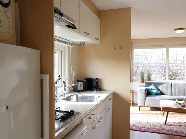 A modern kitchen with a stove, sink, and coffee maker, leading to a living area with a sofa and a coffee table.
