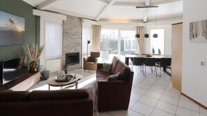 Un grand salon doté d’une cheminée, d’un téléviseur et d’un coin repas avec une table et des chaises.