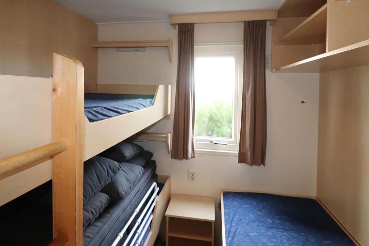 A dormitory room with bunk beds, a small desk, and a window with curtains.