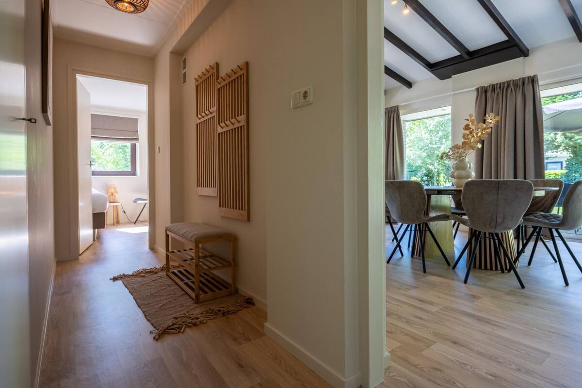 Un interior moderno con piso de madera, un área de comedor con sillas, una mesita y un jarrón decorativo.